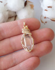 Raw Herkimer diamond pendant shown in hand for size reference, handmade in warm gold copper wire.