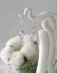 Detailed front view of handcrafted Herkimer diamond sterling silver drop earrings with natural faceted Herkimer diamond, artisan wire wrapping, hanging from a display – Designs by Nature Gems