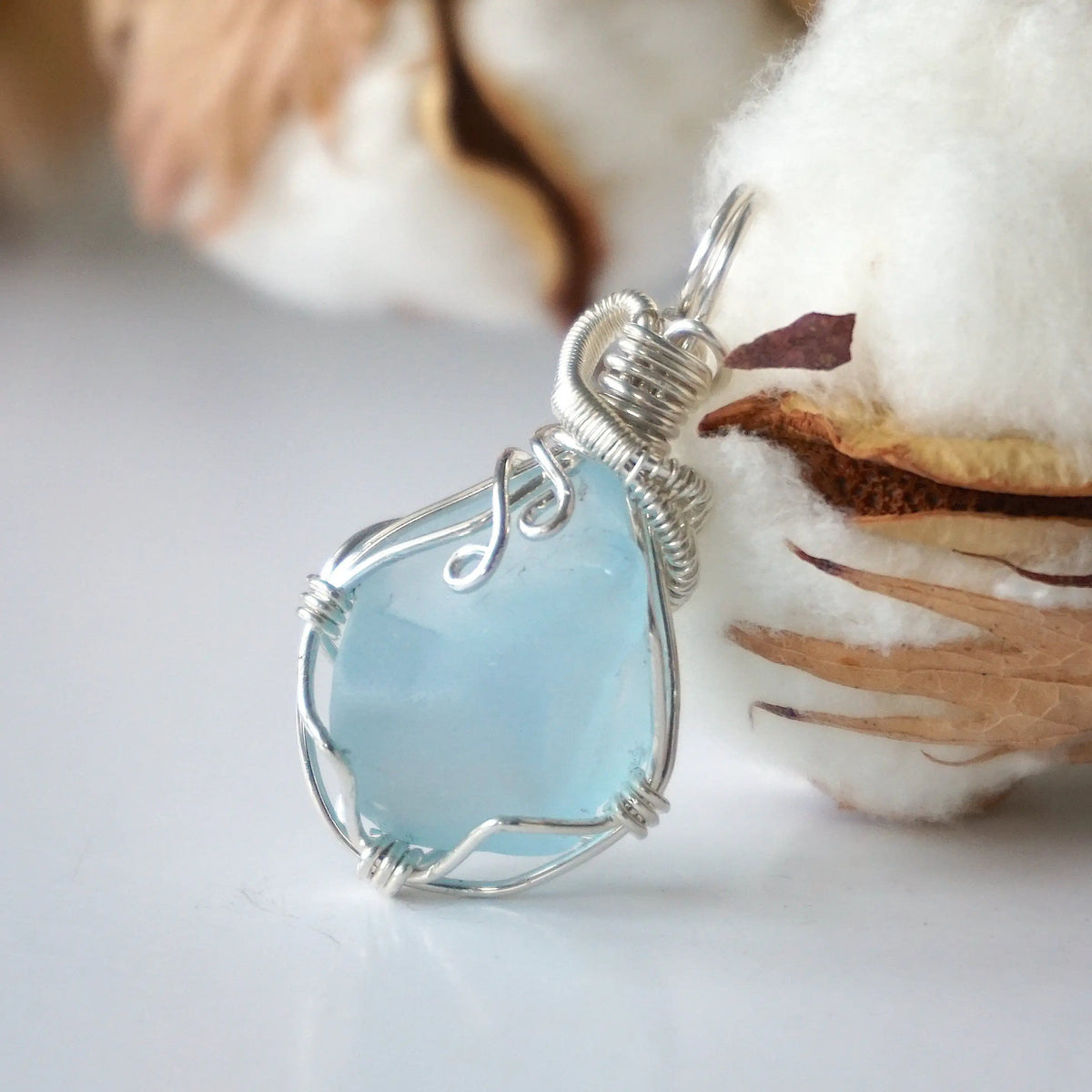 Light blue topaz pendant in sterling silver resting beside a cotton boll