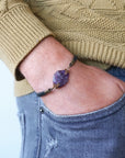 Men’s amethyst bracelet with raw amethyst stone on black leather cord, antique bronze copper wire wrapped, shown on model’s wrist
