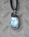 Detailed front angle of men's aquamarine pendant on a black leather cord, artisan wire wrapped in black and white gold finish