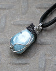 Detailed left side angle of men's aquamarine pendant on a black leather cord, black and white gold finish wire wrapping