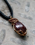 Right side angle view of a men’s garnet wire wrapped pendant in antique bronze copper on a black leather cord