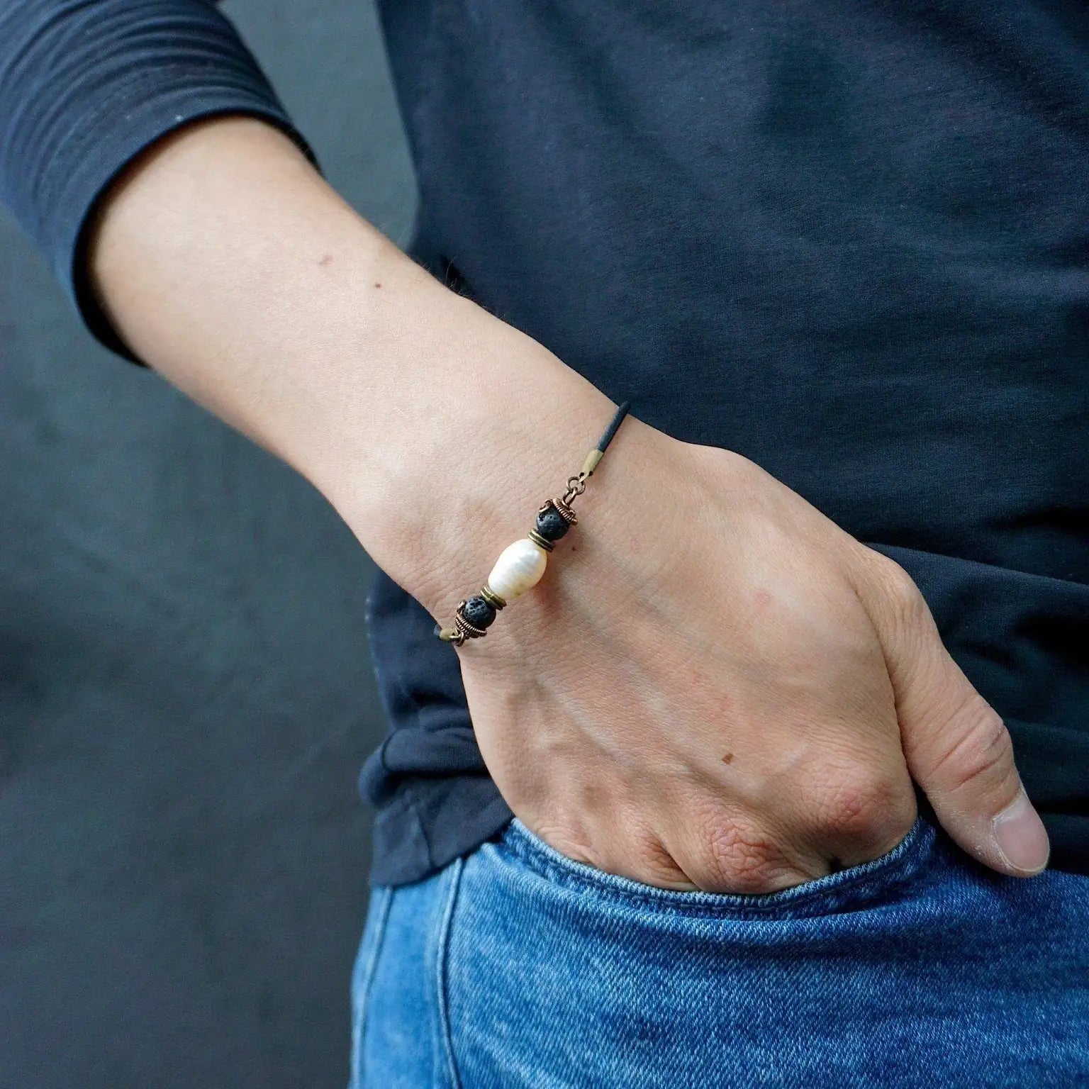 Close-up of a men’s pearl leather bracelet with lava stone accents worn on a model’s wrist