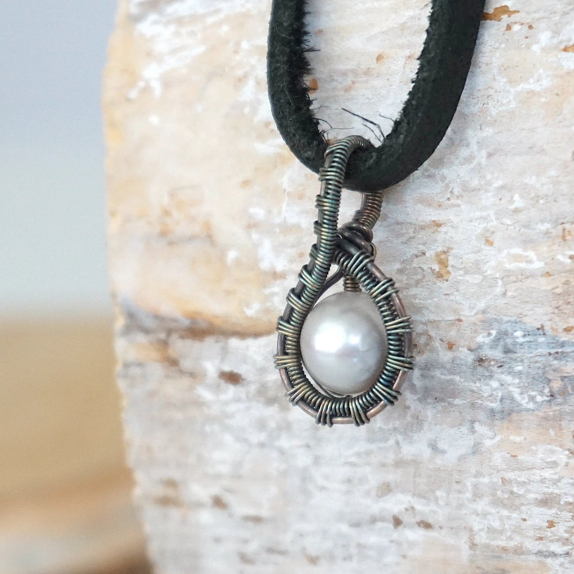 Side angle view of a men’s pearl pendant necklace wrapped in antiqued sterling silver on a black leather cord