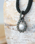 Side angle view of a men’s pearl pendant necklace wrapped in antiqued sterling silver on a black leather cord
