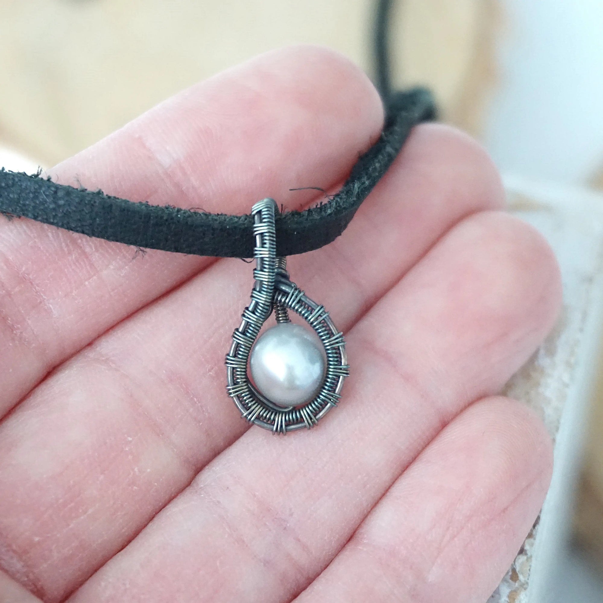 Men’s pearl pendant necklace shown in hand for size reference, featuring an antiqued sterling silver wrapped pearl