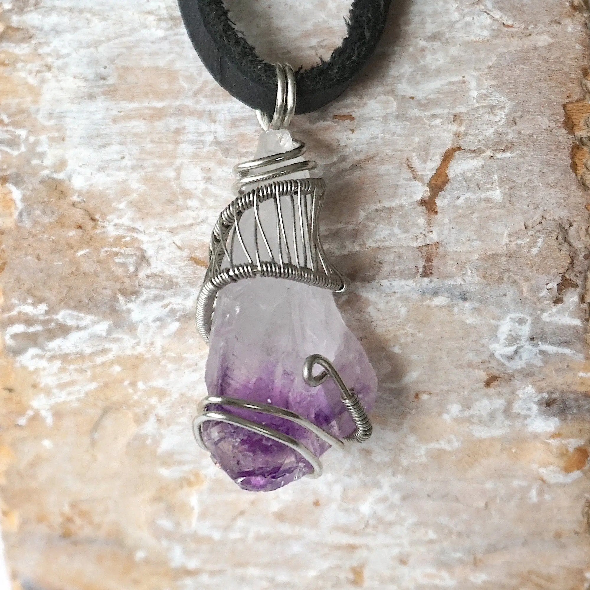 Back side angle of men’s raw amethyst pendant wire wrapped in white gold plated copper on black leather cord