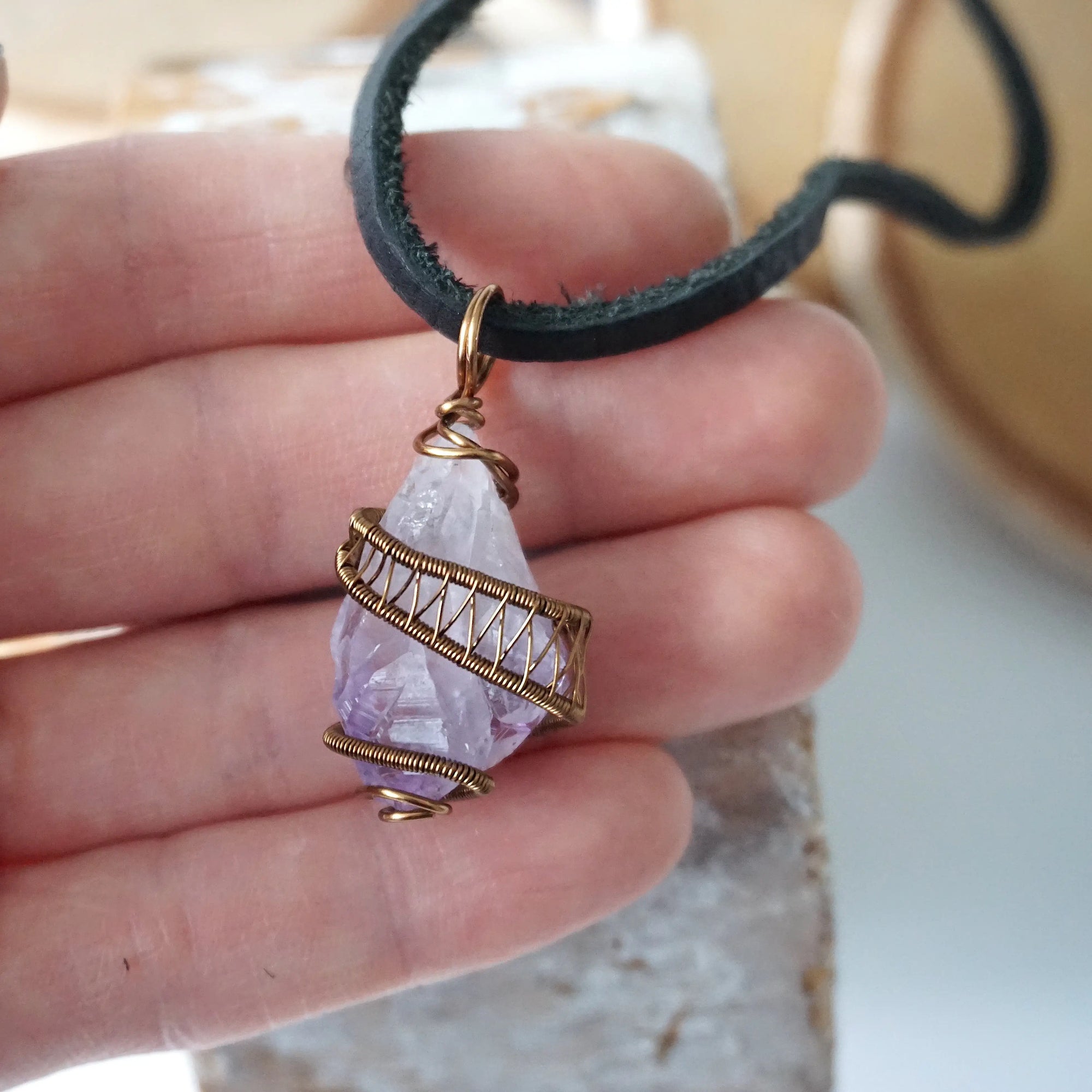 Men’s raw amethyst pendant on black leather cord shown in hand for size reference, antique bronze copper wire wrapped crystal necklace