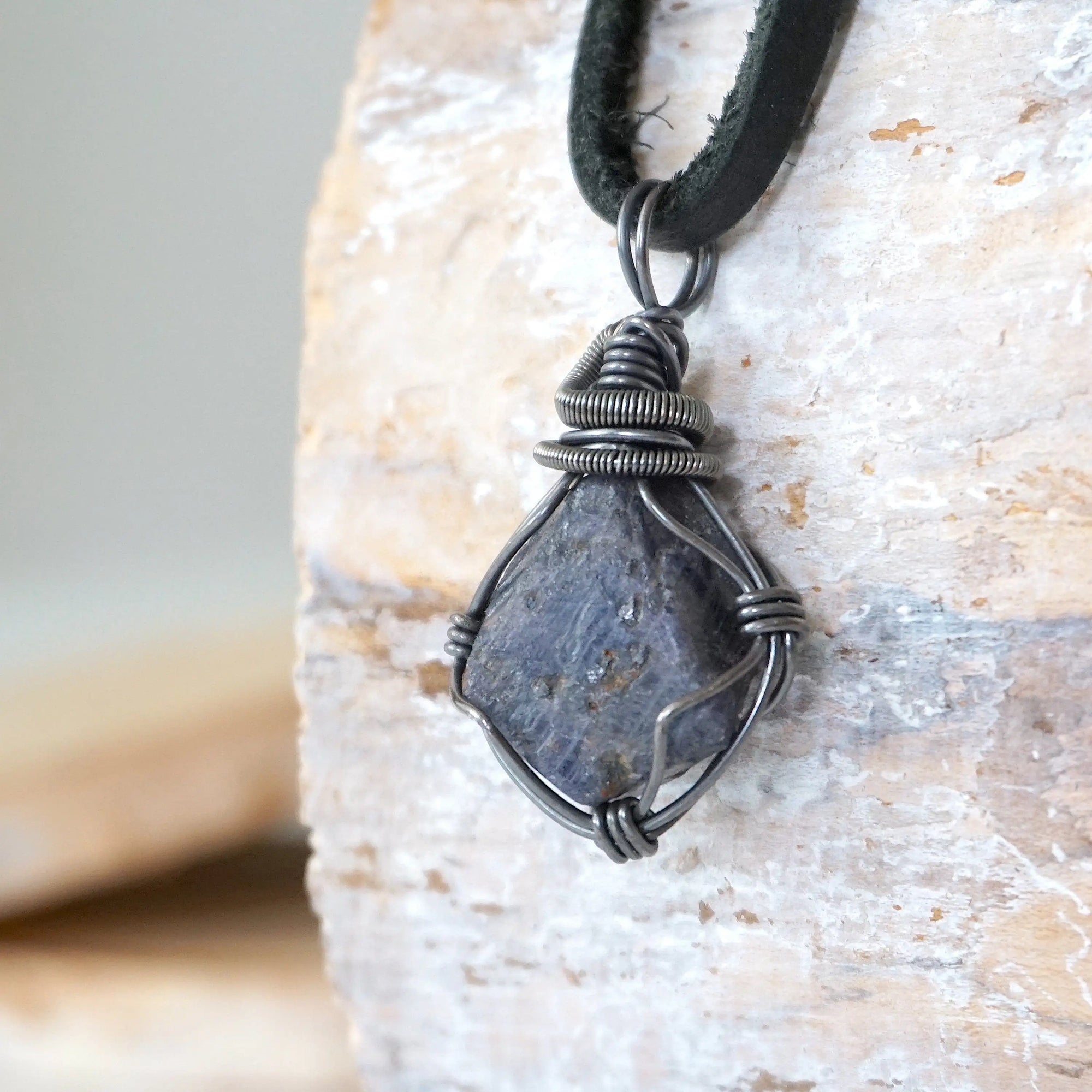 Left-angle close-up of raw sapphire pendant revealing the precision of antiqued sterling silver wire-wrapping craftsmanship — men's artisan crystal jewelry