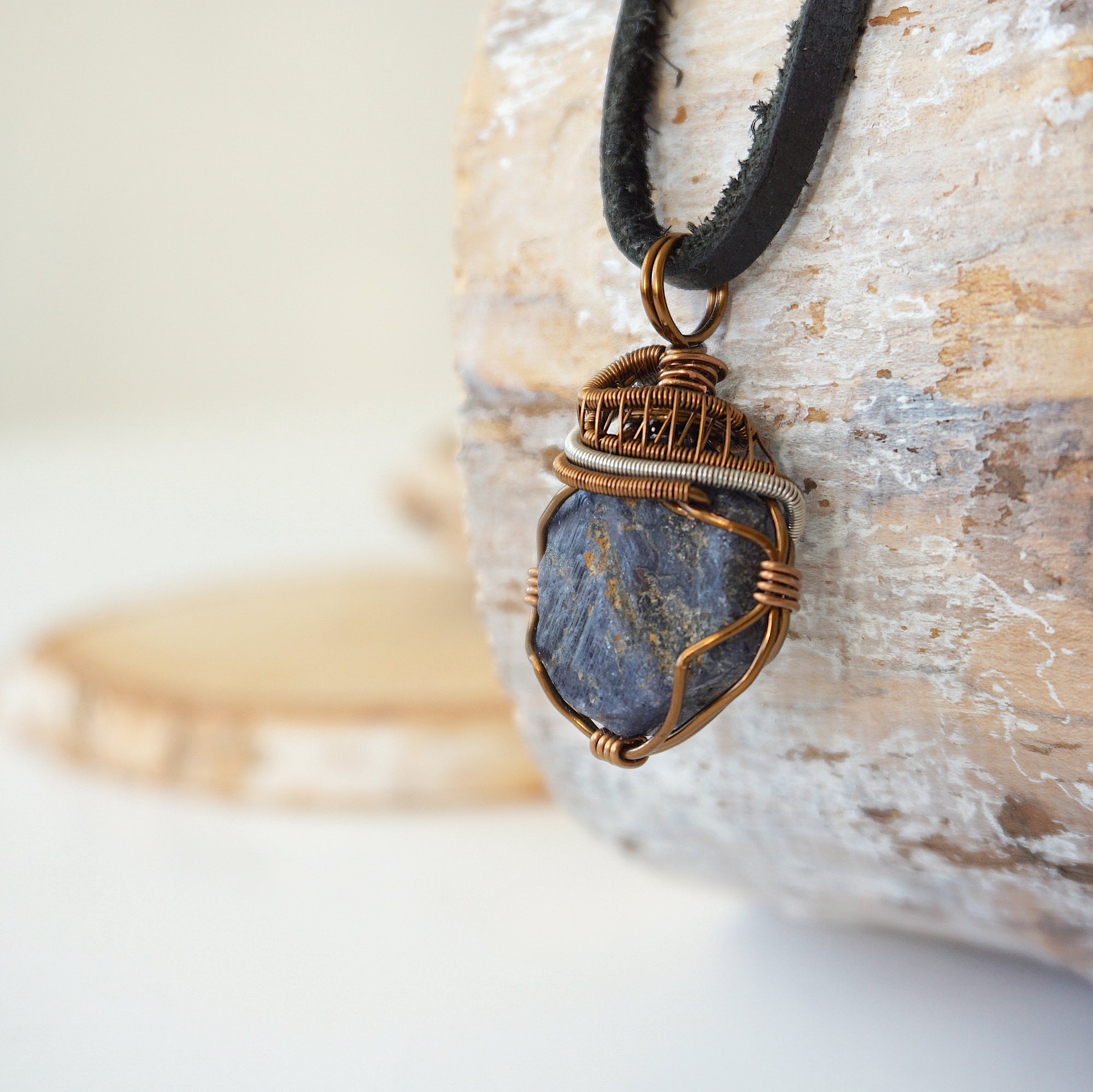 Left-angle close-up of raw sapphire pendant revealing the dual-metal wire-wrapping craftsmanship in antique bronze and dark silver