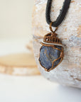 Left-angle close-up of raw sapphire pendant revealing the dual-metal wire-wrapping craftsmanship in antique bronze and dark silver