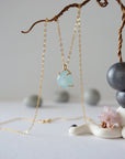 Zoomed out view of minimalist aquamarine necklace in gold, hanging on display, artisan claw setting, gold filled chain