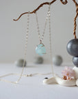 Zoomed out view of minimalist aquamarine necklace hanging on display, artisan claw setting, sterling silver chain