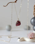 Side view of minimalist garnet pendant showing sterling silver claw setting and raw garnet texture on silver chain