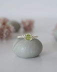 Front view of minimalist silver wire wrapped peridot ring — faceted 5mm olive green peridot bead, dainty handcrafted August birthstone crystal ring for women