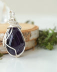 Right side view detail of polished dark amethyst pendant with silver plated copper wire wrapping, handmade necklace
