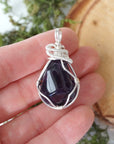 Natural dark amethyst pendant held in hand for size reference, handmade sterling silver wire wrapped necklace