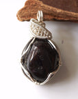 Detailed front view of natural raw garnet pendant with intricate silver plated copper wire wrapping