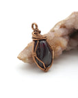 Side angle view of natural garnet pendant with simple antique bronze copper wire wrapping