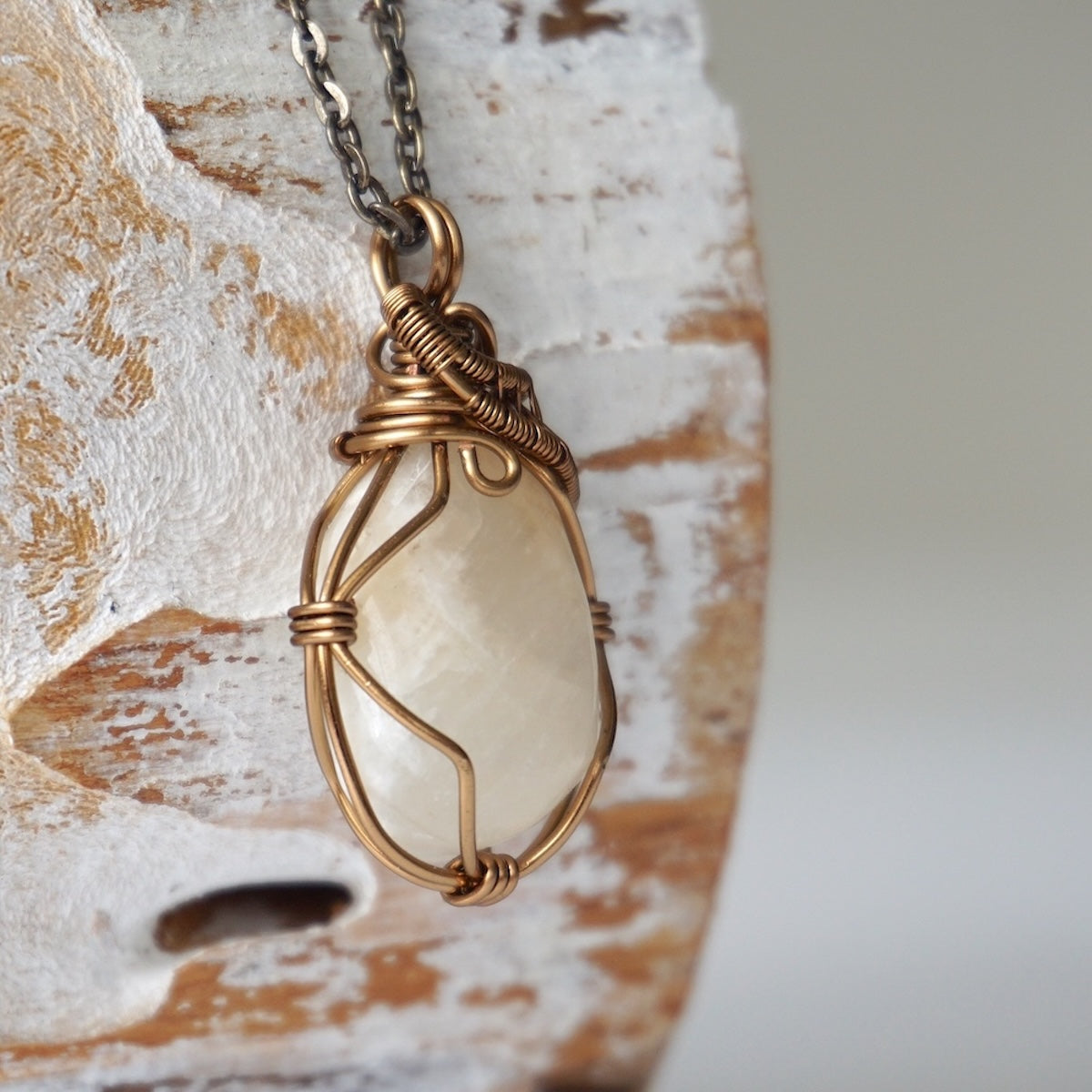 Right angle close-up of polished-raw moonstone pendant with detailed artisan antique bronze wire wrapping on cable chain.