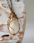 Right angle close-up of polished-raw moonstone pendant with detailed artisan antique bronze wire wrapping on cable chain.