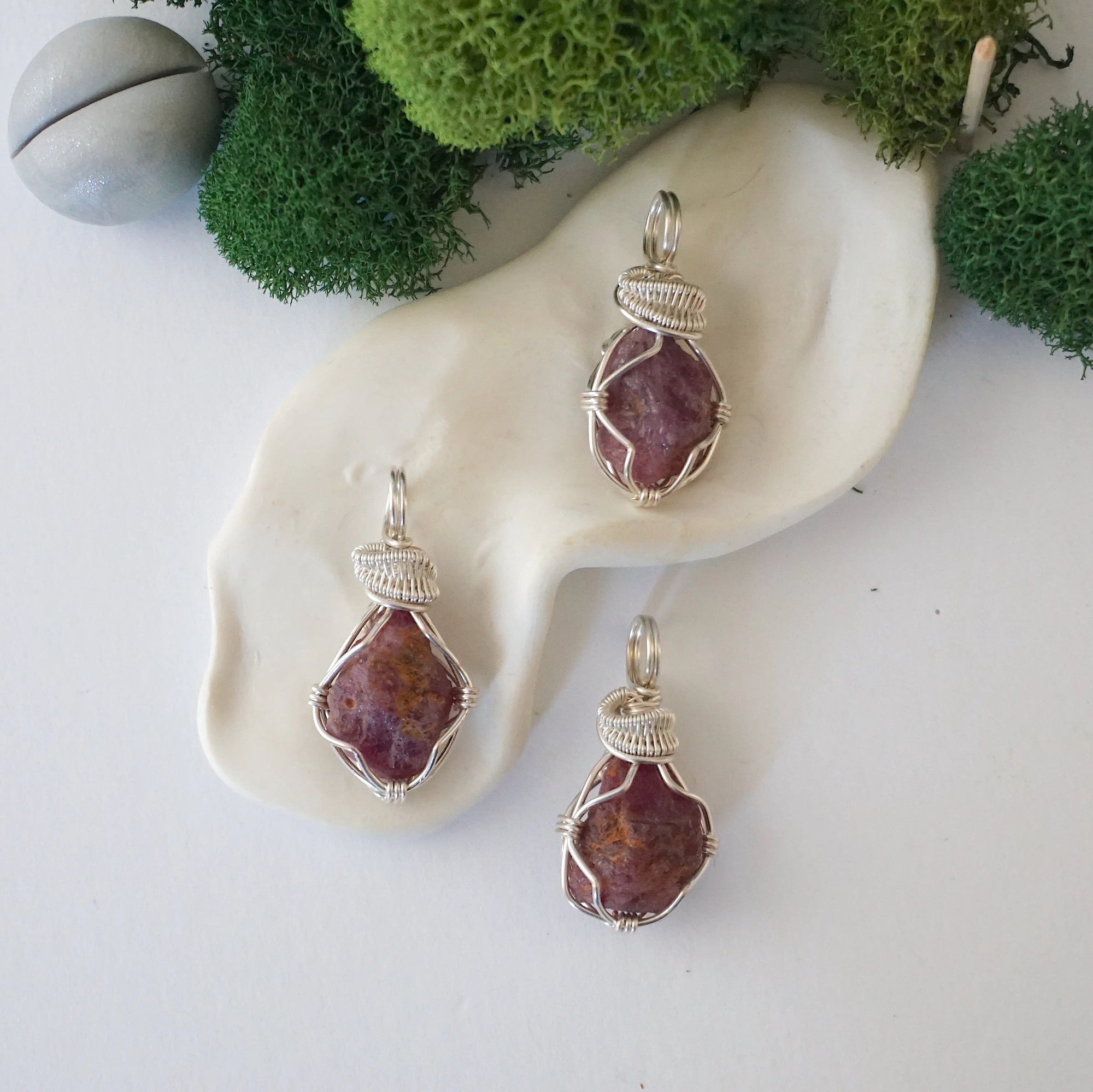 Three natural raw ruby pendants side by side showing unique variation in size, shape, and colour — each one of a kind by nature