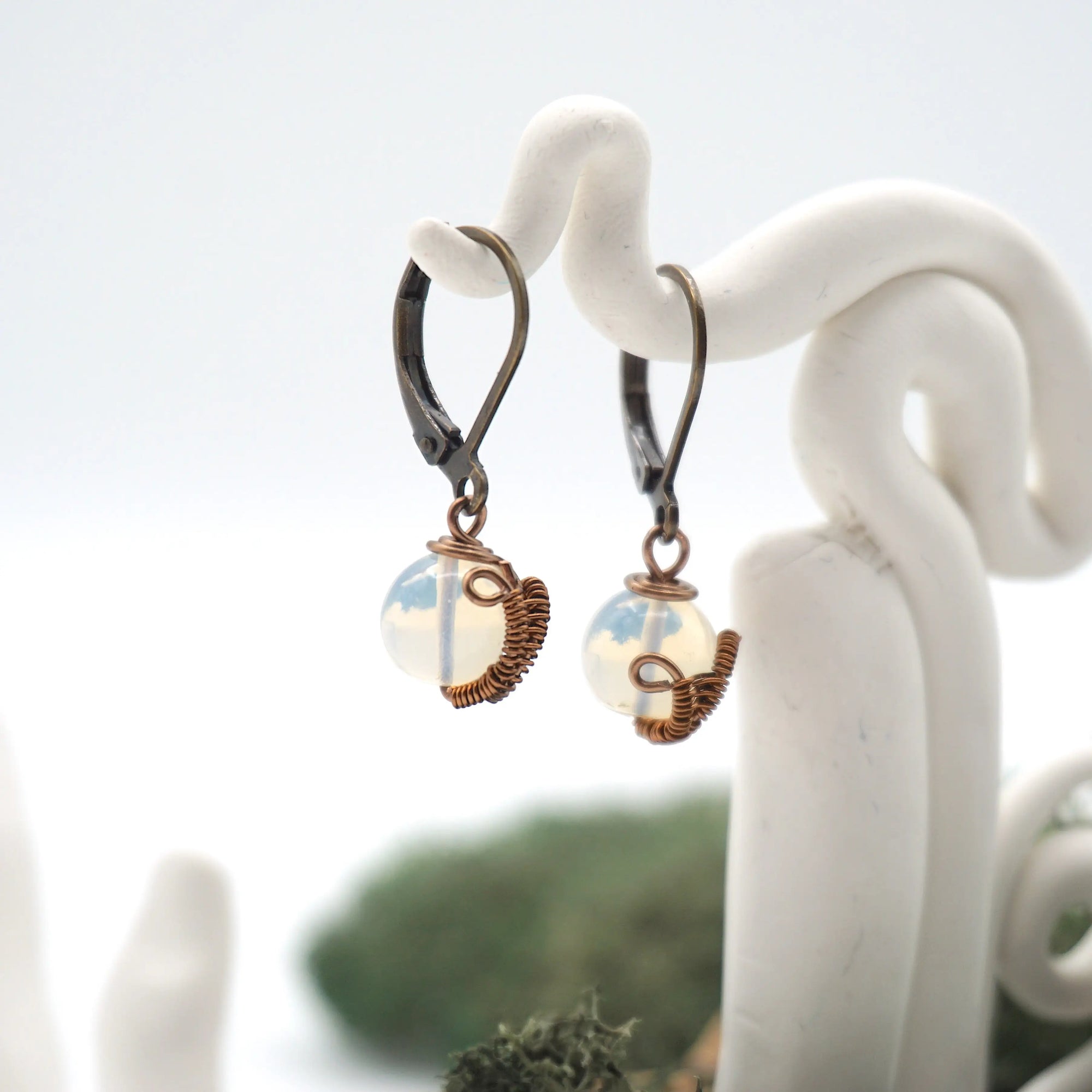 Side angle of opal drop earrings on a display stand, highlighting antique bronze copper wire wrapping.