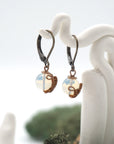 Side angle of opal drop earrings on a display stand, highlighting antique bronze copper wire wrapping.