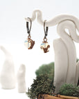 Front angle of opal drop earrings hanging on a jewelry display, wire-wrapped design.