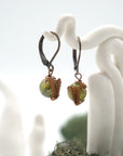 Side angle of peridot drop earrings on a display stand, highlighting antique bronze copper wire wrapping.