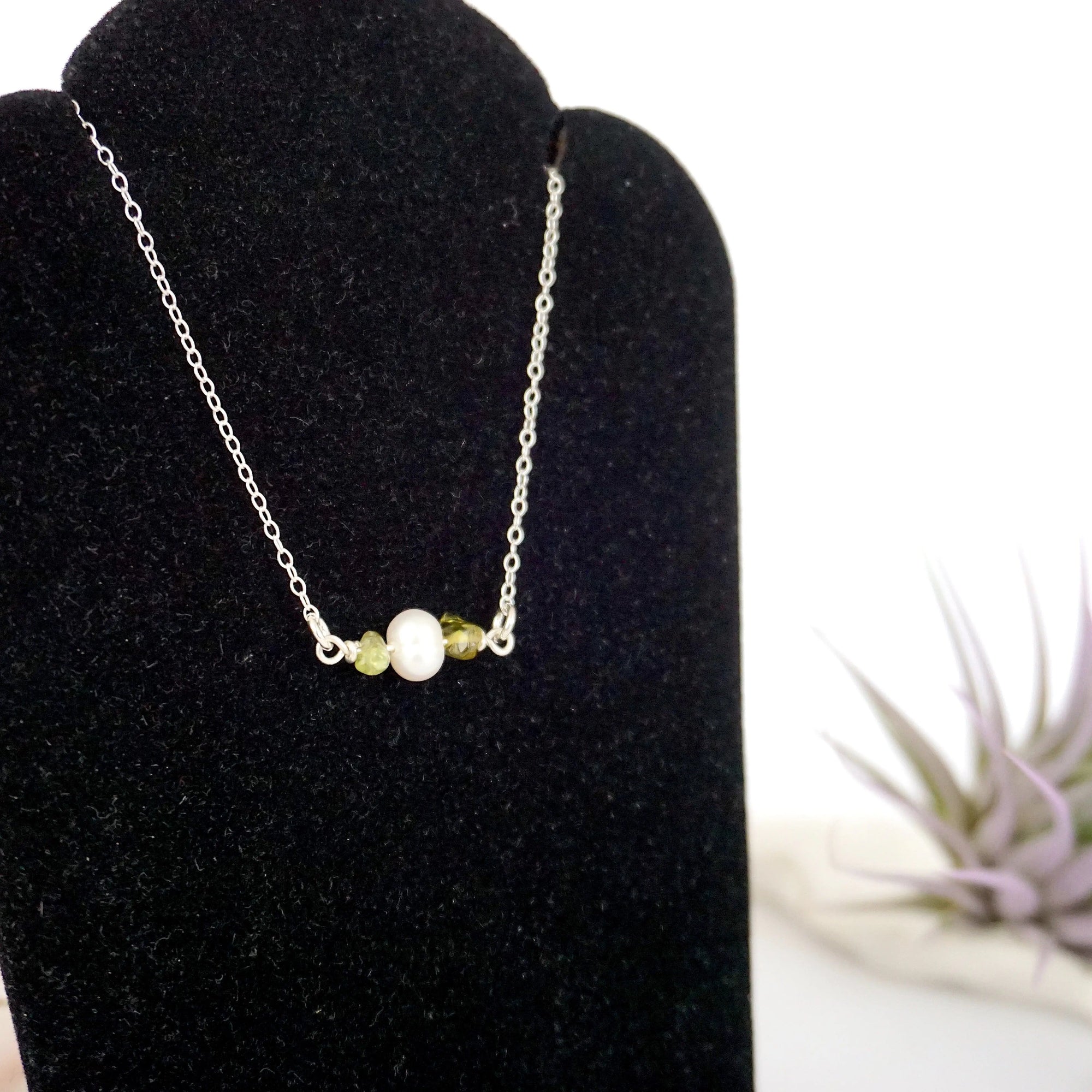 Focused left-side close-up of sterling silver peridot and pearl bar necklace on jewelry display