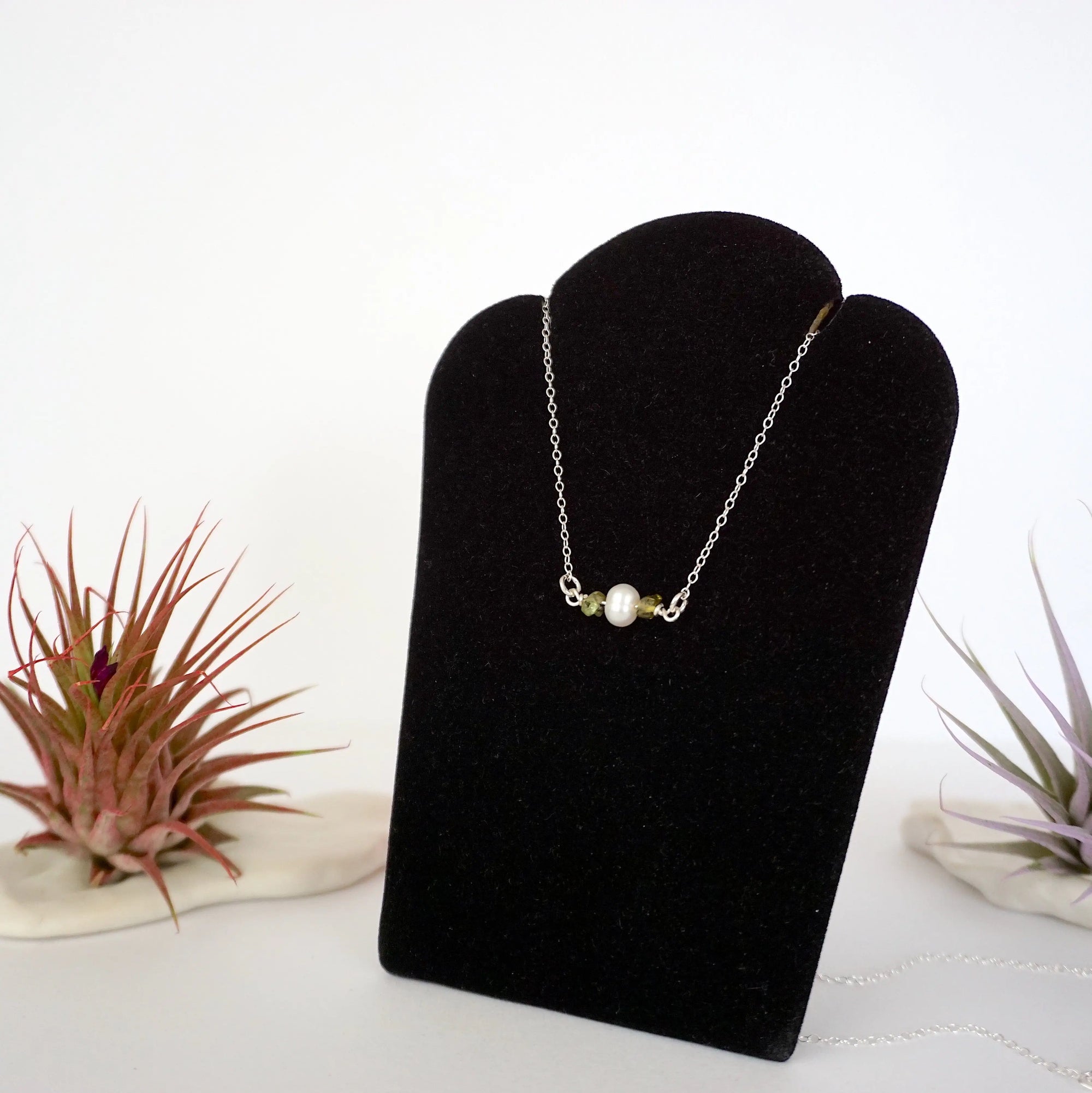 Left angle view of peridot and pearl bar necklace in 925 sterling silver on jewelry display
