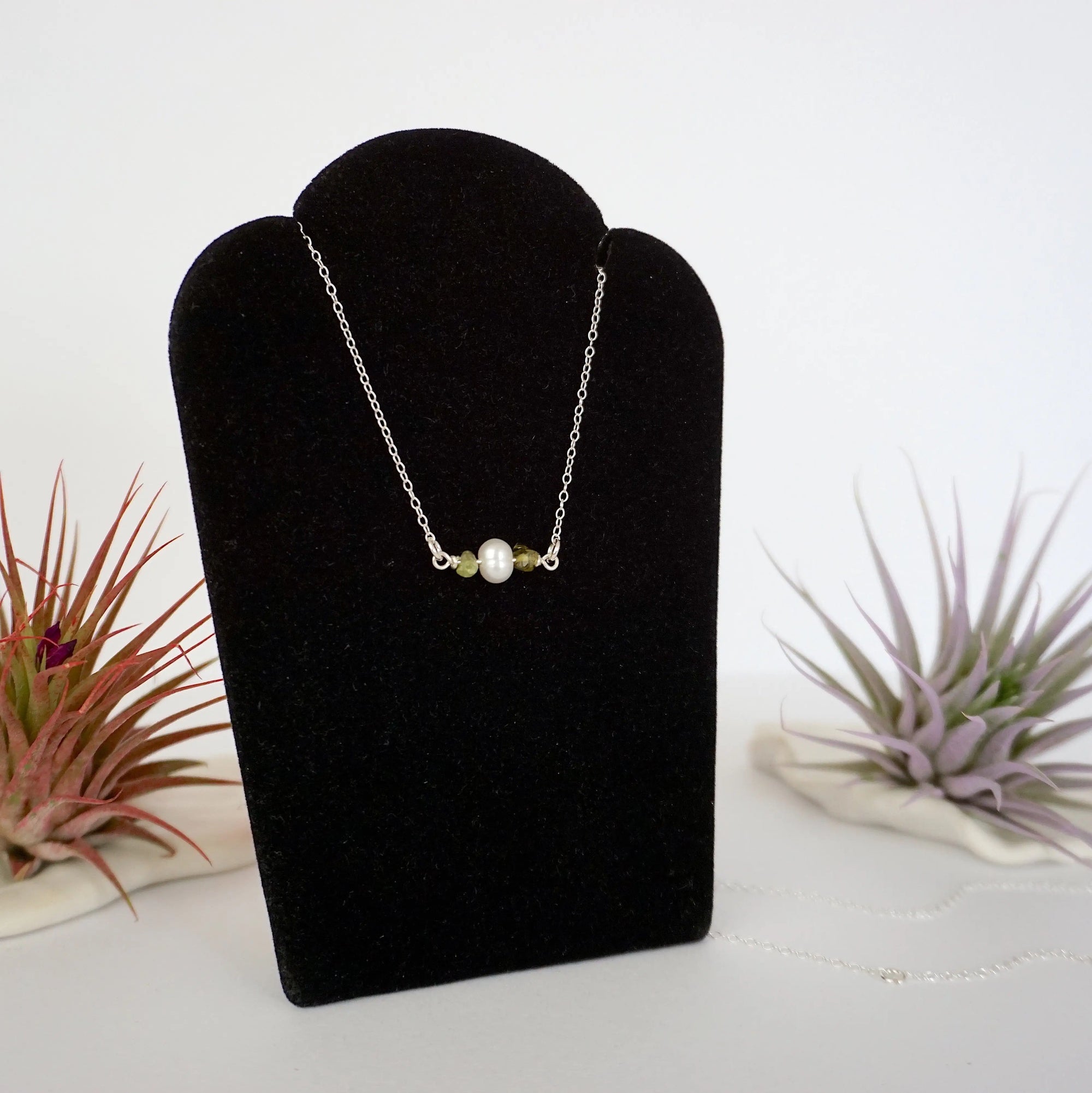 Right angle view of peridot and freshwater pearl bar necklace in 925 sterling silver on jewelry display