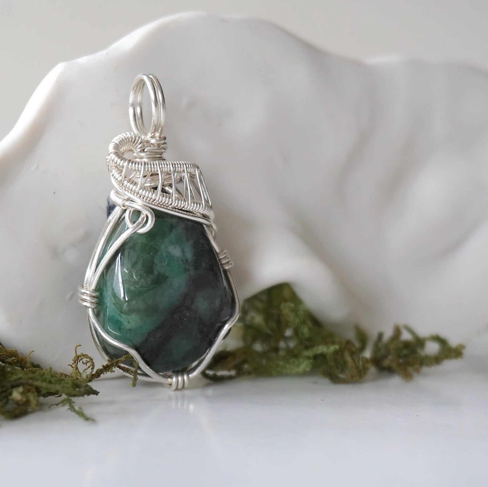 Right angle detail of polished raw emerald pendant for women showing natural emerald and artisan 925 sterling silver wire wrapping