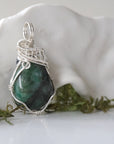 Right angle detail of polished raw emerald pendant for women showing natural emerald and artisan 925 sterling silver wire wrapping