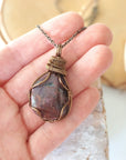 Large polished raw ruby pendant held in hand to show size — 100 to 120 carat natural ruby in antique bronze wire wrapping, men's statement crystal necklace