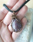 Large polished raw ruby pendant held in hand to show size — 100 to 120 carat natural ruby in antique bronze wire wrapping, men's statement crystal necklace
