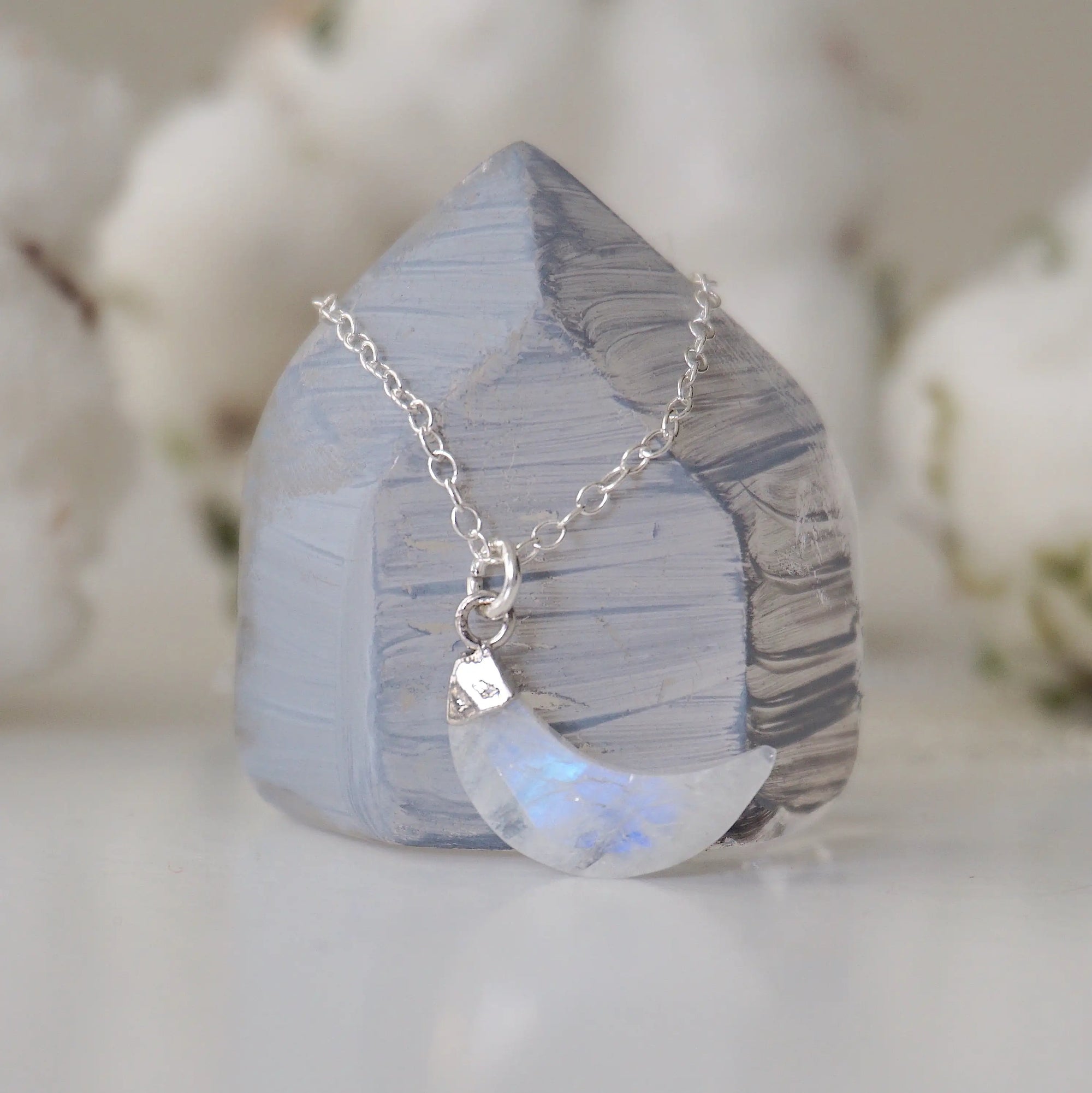 Side angle close-up of faceted rainbow moonstone crescent moon pendant in 925 sterling silver setting on sterling silver chain, June birthstone necklace.