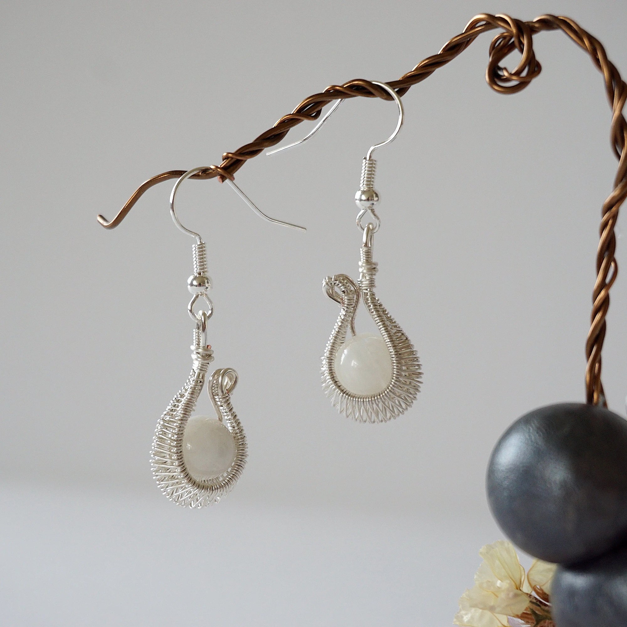 Side angle close-up of wire wrapped rainbow moonstone drop earrings highlighting pendant profile, soft silver finish, and June birthstone stone.