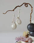 Macro close-up showing detailed artisan wire wrapping in soft silver copper around natural rainbow moonstone bead on drop earrings.