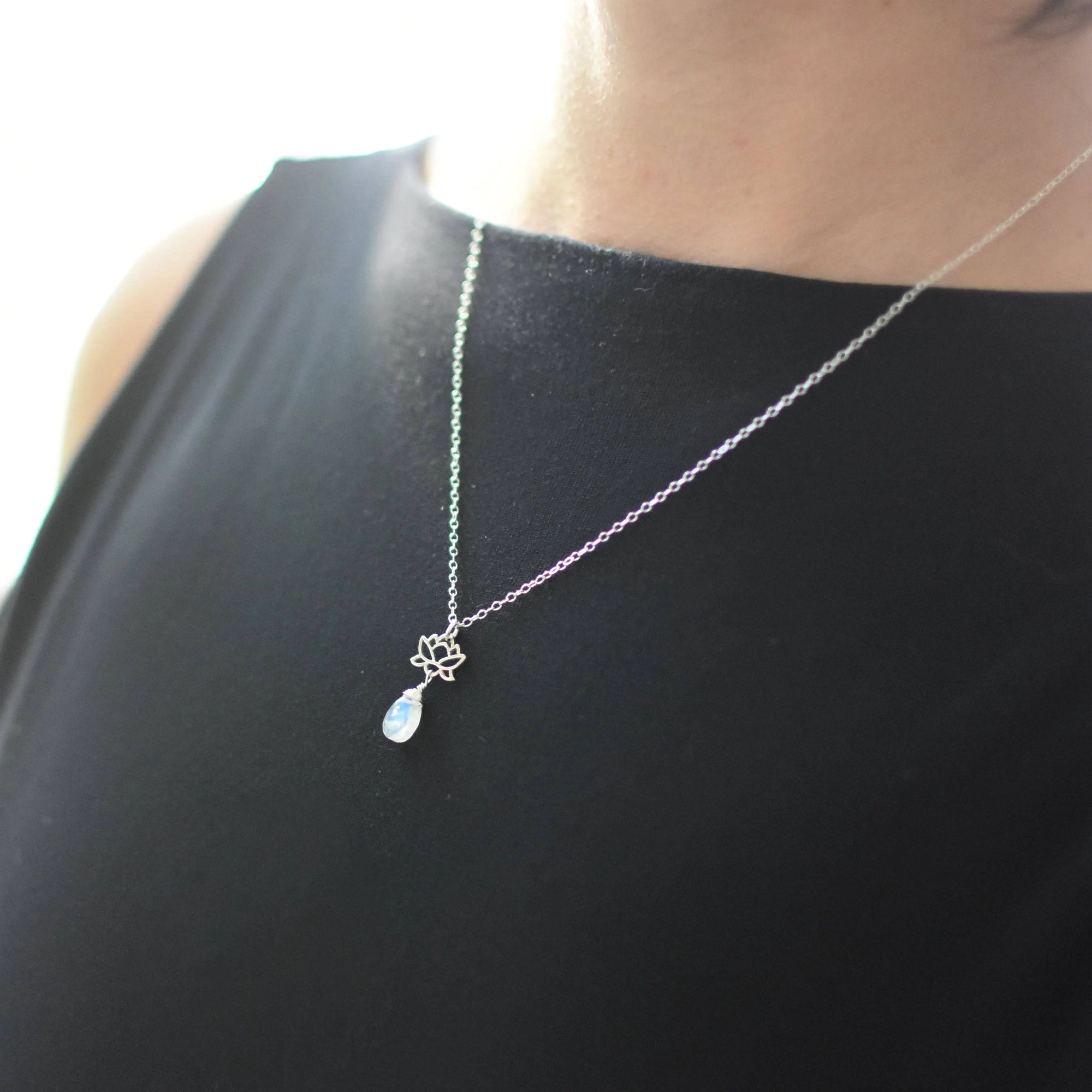 Rainbow moonstone and lotus necklace worn on a female model, faceted pear moonstone pendant with 925 sterling silver lotus charm on sterling silver chain.