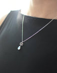 Rainbow moonstone and lotus necklace worn on a female model, faceted pear moonstone pendant with 925 sterling silver lotus charm on sterling silver chain.