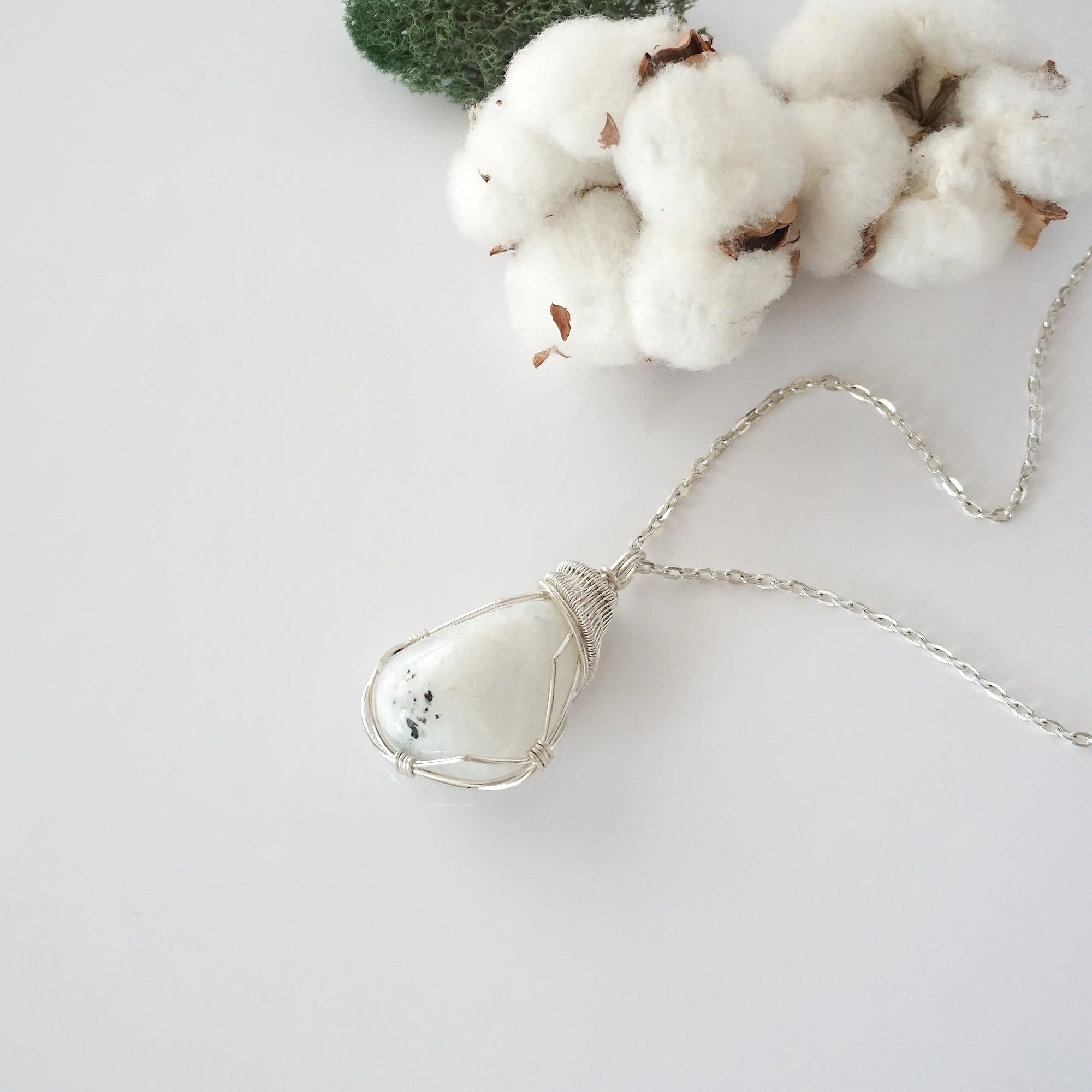Rainbow moonstone necklace displayed on flat surface with natural polished-raw stone and soft silver wire wrapping