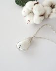 Rainbow moonstone necklace displayed on flat surface with natural polished-raw stone and soft silver wire wrapping
