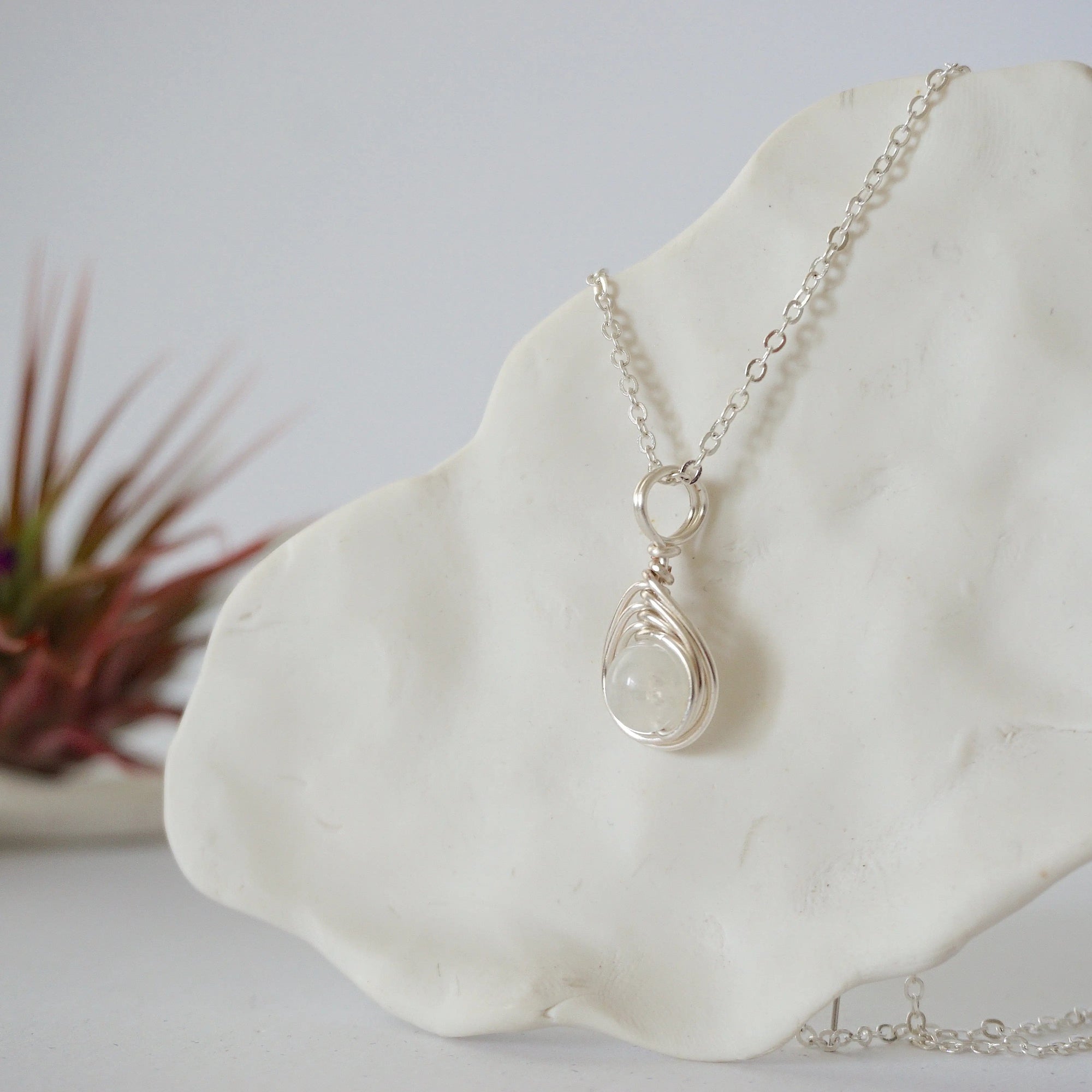 Left side angle close-up of minimalist rainbow moonstone bead necklace highlighting handcrafted soft silver wire wrap and pendant profile.