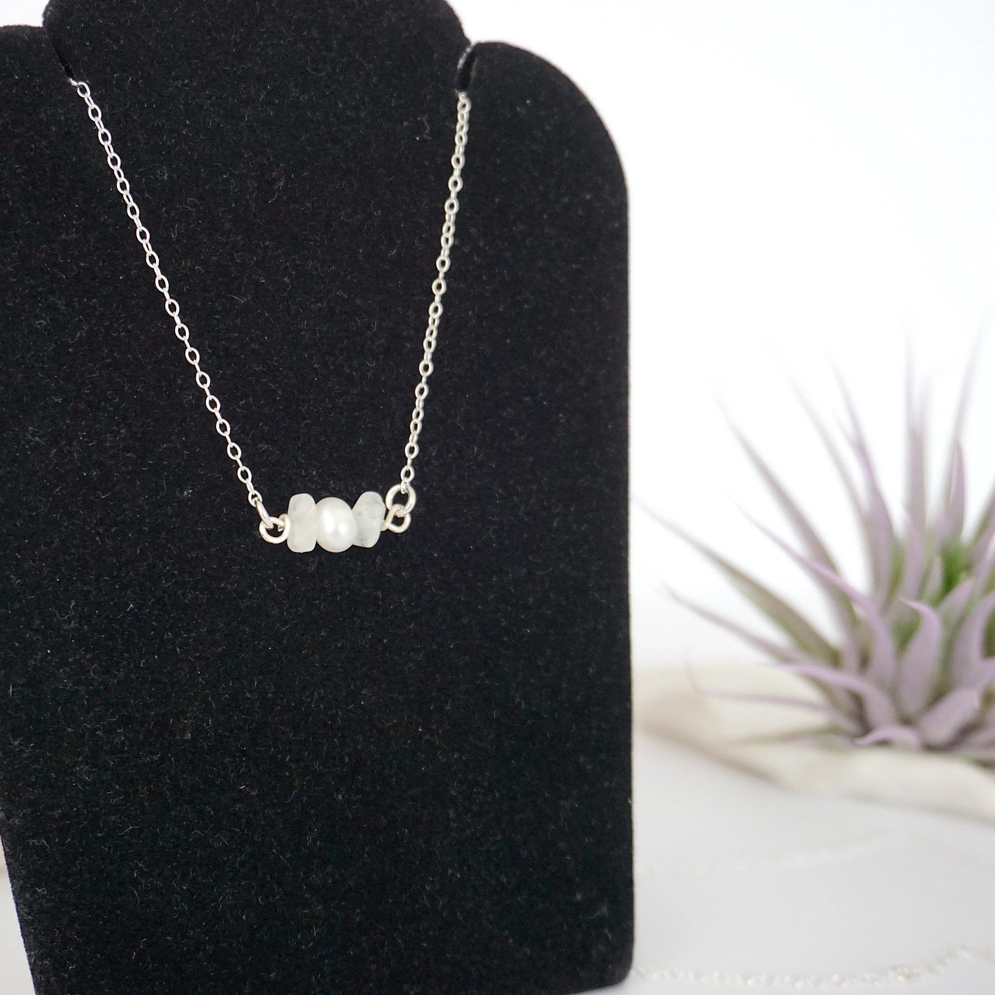 Focused left-side close-up of sterling silver rainbow moonstone and pearl bar necklace on jewelry display