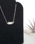 Focused left-side close-up of sterling silver rainbow moonstone and pearl bar necklace on jewelry display