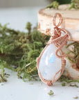 Angled close-up of natural rainbow moonstone cabochon pendant with detailed 14k rose gold filled wire wrapping