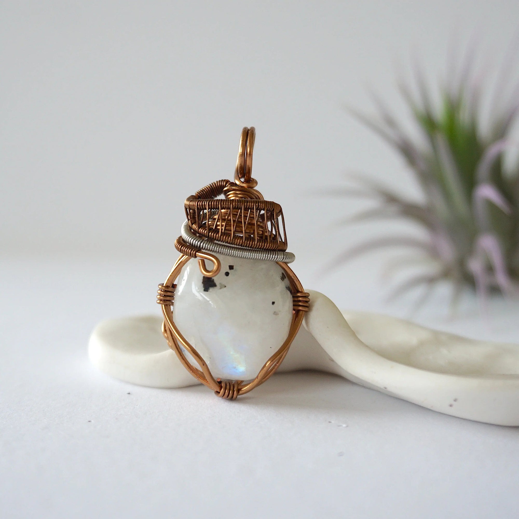 Front angle view of natural rainbow moonstone pendant with detailed antique bronze and dark silver wire wrapping